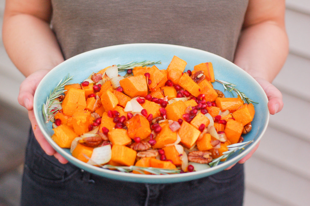 beautiful photo of a thanksgiving side dish made with orange butternut squash, red pomegranate seeds, walnuts, and sprigs of rosemary